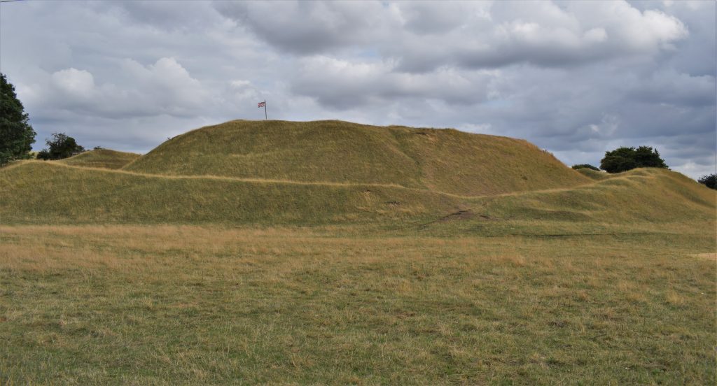 Bytham Castle earthworks, grass covered mounds. The central mound appears like a hill with a flat top, and is surrounded by a ditch and bank.