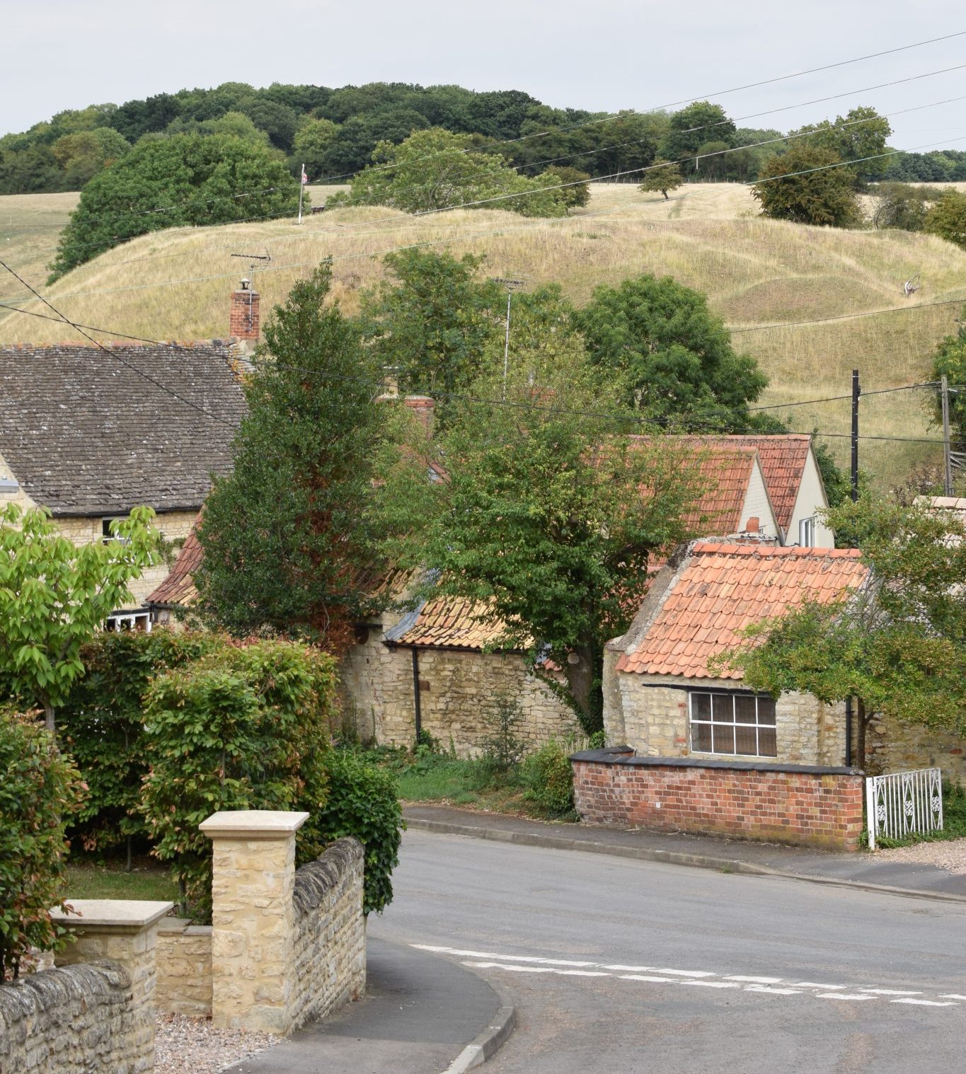 Village scene showing the earthworks of Bytham Castle rising up behind stone built houses and partially obscured by trees
