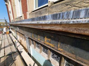 Shopfront during restoration with faint signage reading 'Clothiers & Outfitters in gold leaf